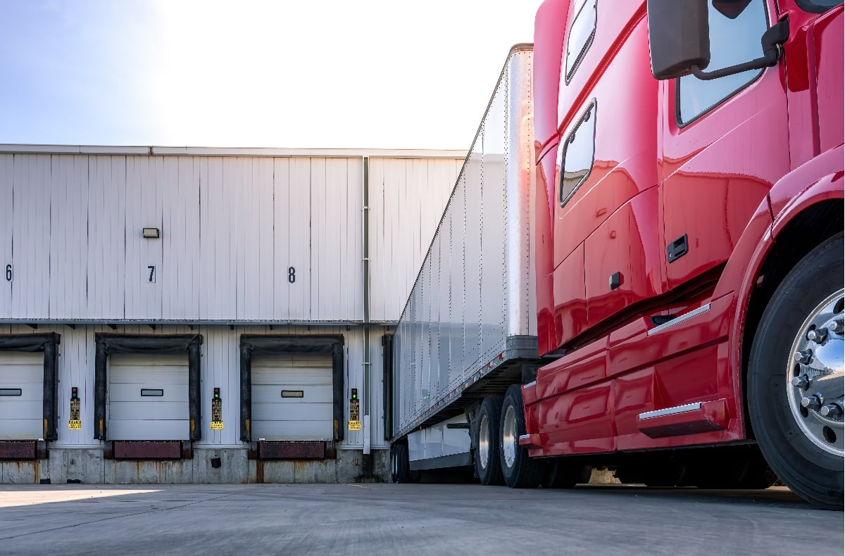 A red semi truck unloads cargo at a distribution center.